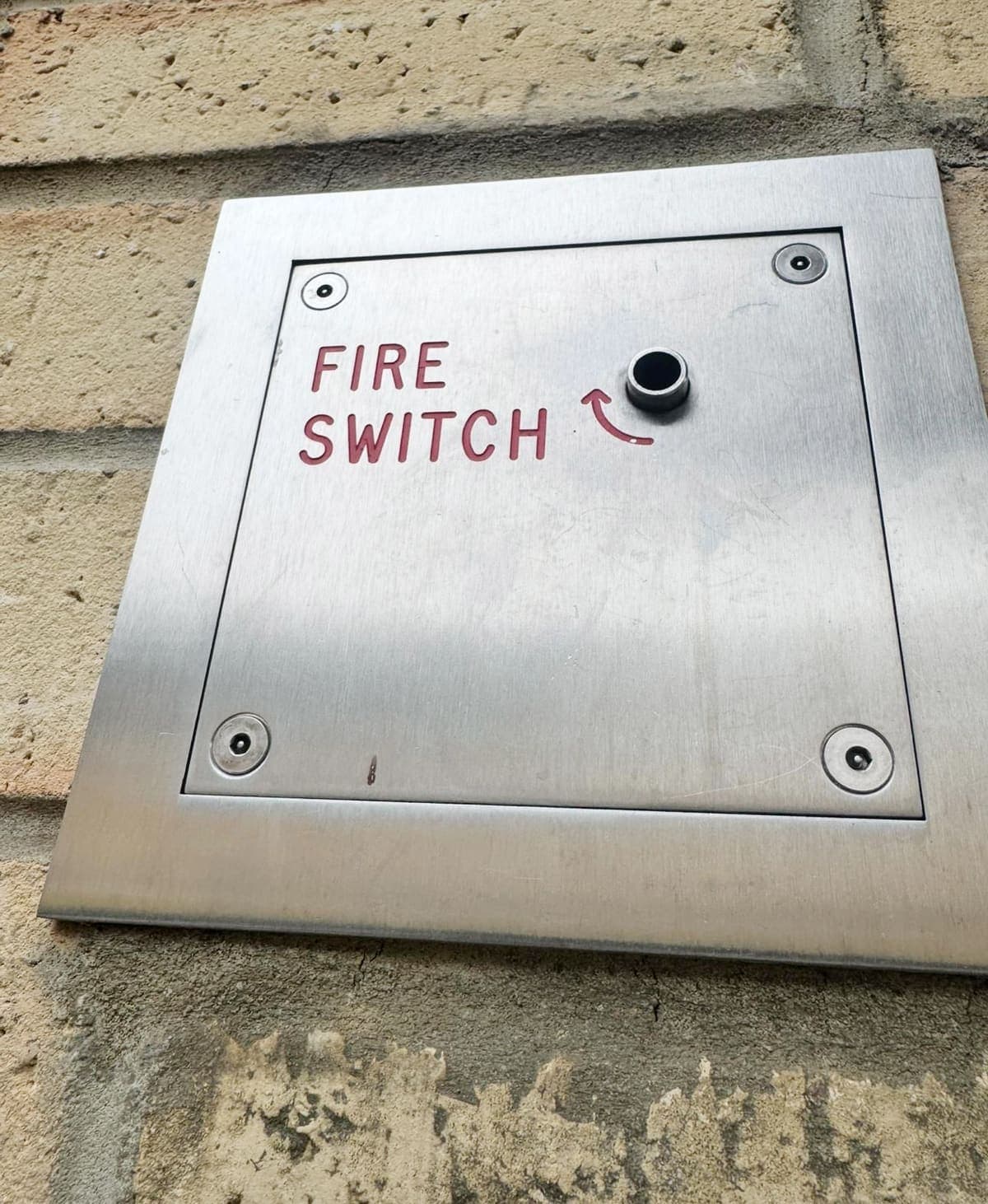 A stainless steel fire switch plate mounted on a brick wall